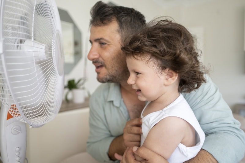 father and toddler in front of a fan in living room.